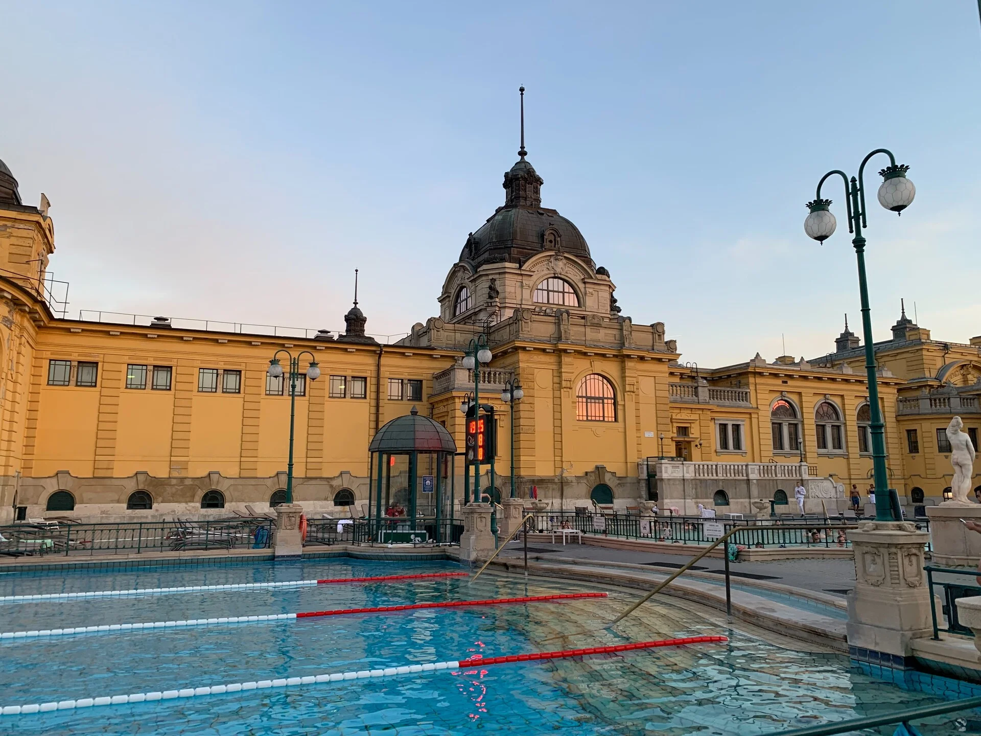 Piscinas ao ar livre dos Banhos Termais Szechenyi em Budapeste com o iconico edificio neobarroco amarelo e vapor subindo da agua
