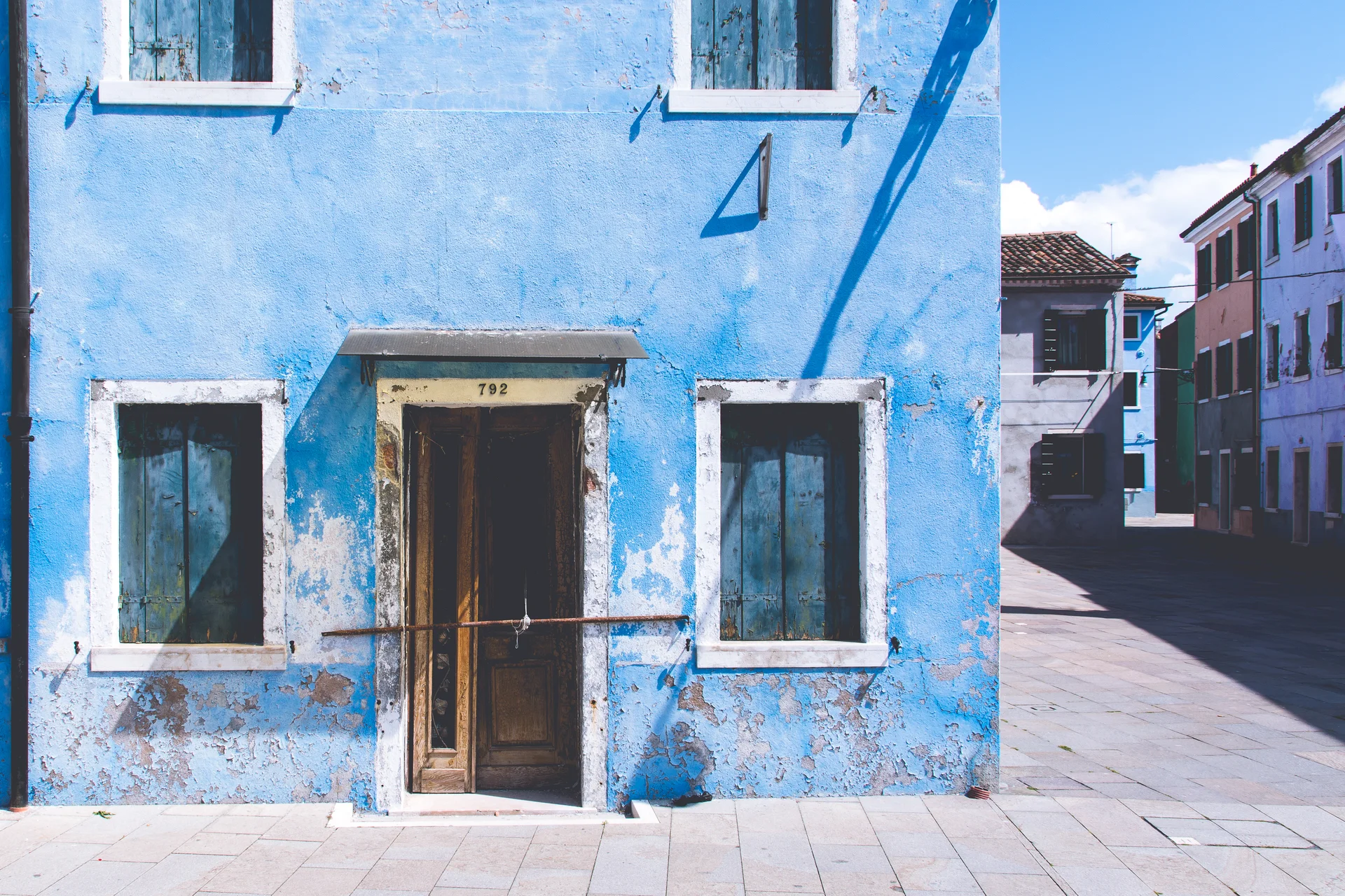 Uma casa pintada de azul vivo na ilha de Burano, na lagoa de Veneza, com outras casas coloridas ao fundo