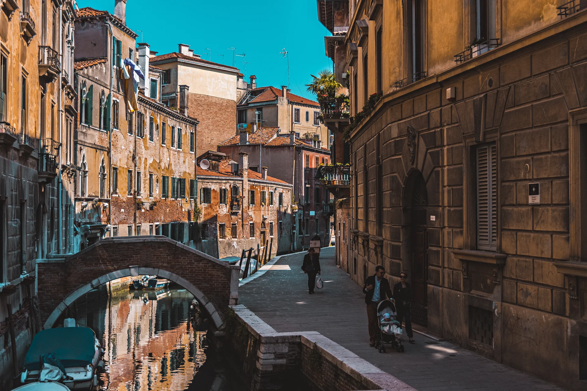 Um canal veneziano banhado pelo sol com uma ponte de pedra, táxis aquáticos e edifícios históricos perto do Grande Canal em Veneza