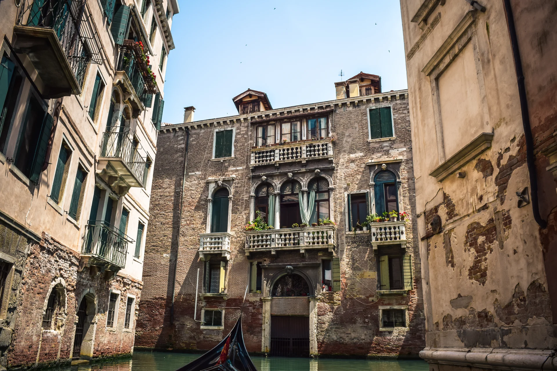 Um canal lateral tranquilo de Veneza ladeado por palazzi desgastados e uma única gôndola deslizando em direção a uma ponte de pedra