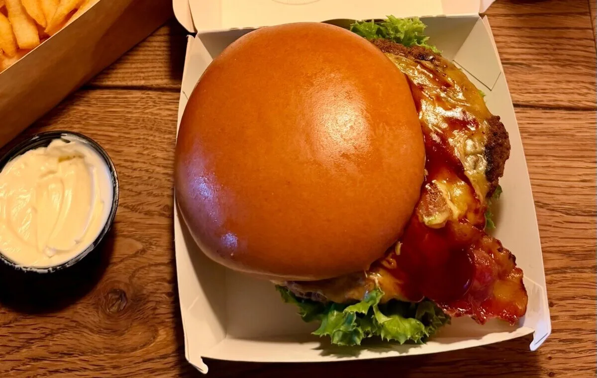 A bacon cheeseburger in a cardboard box with fries and a dip at a burger bar in Copenhagen