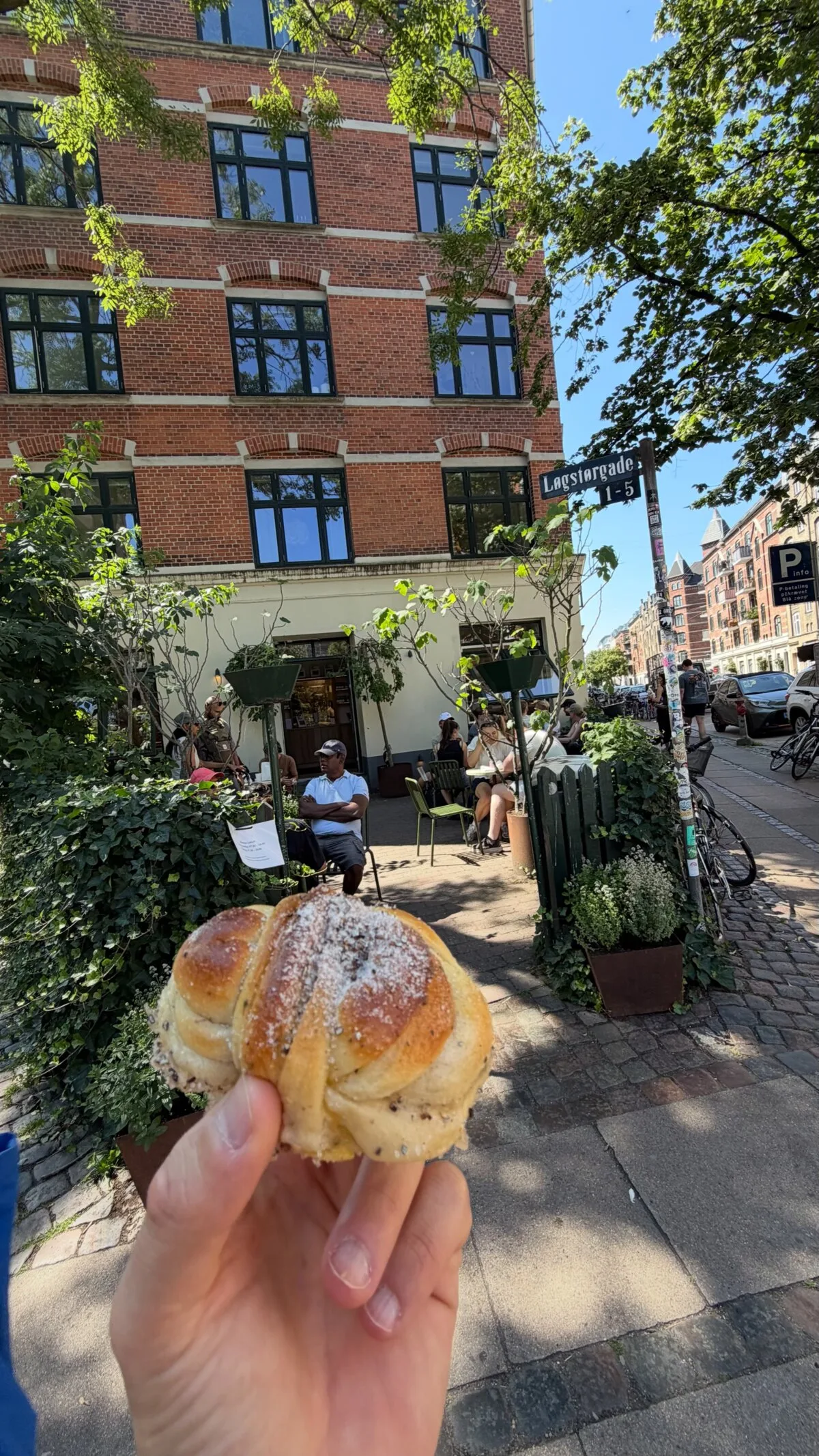 Holding a cardamom bun from Juno the Bakery on a leafy street in Copenhagen