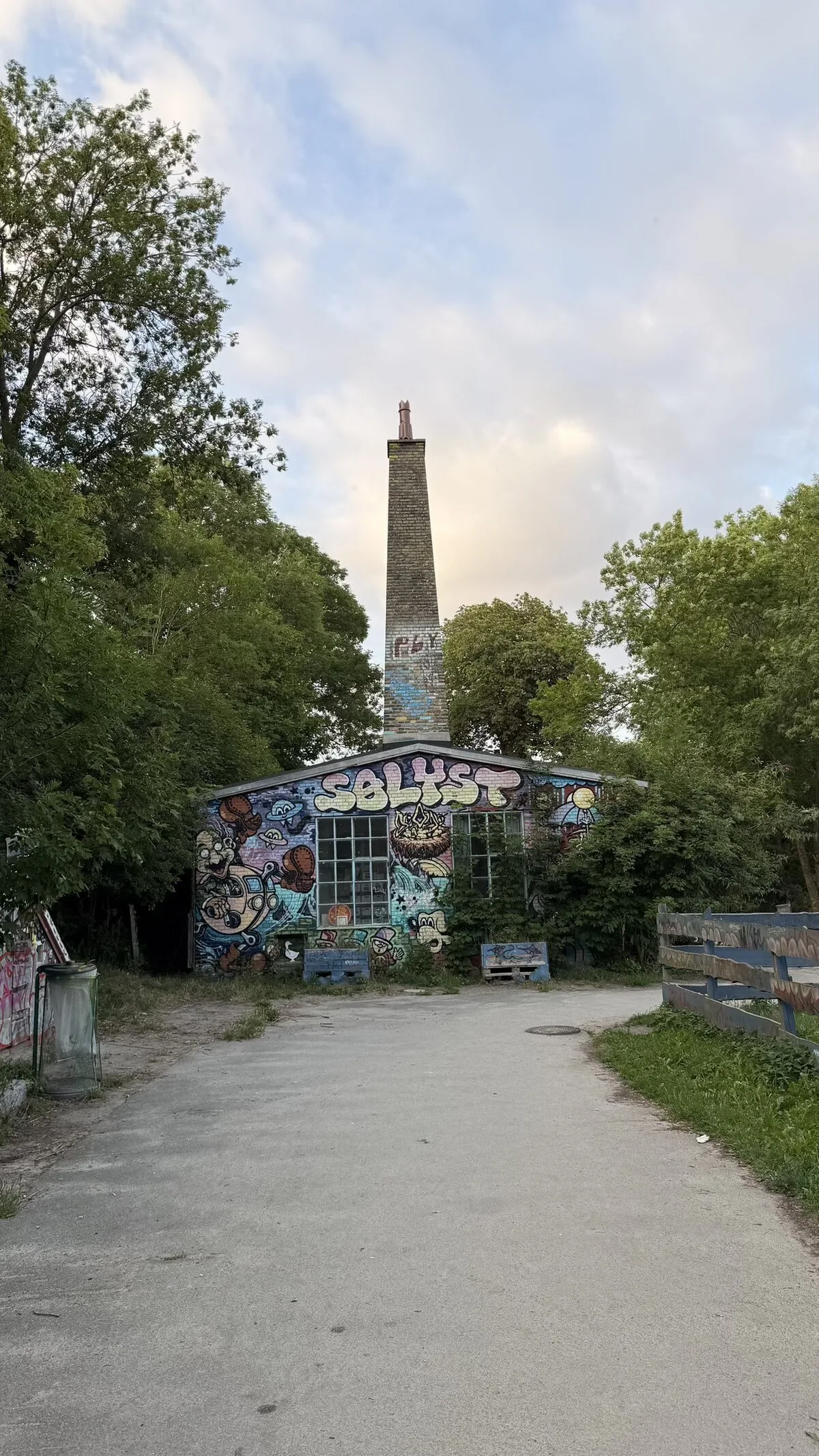 A path in Freetown Christiania, Copenhagen, lined with trees and a colourfully painted building