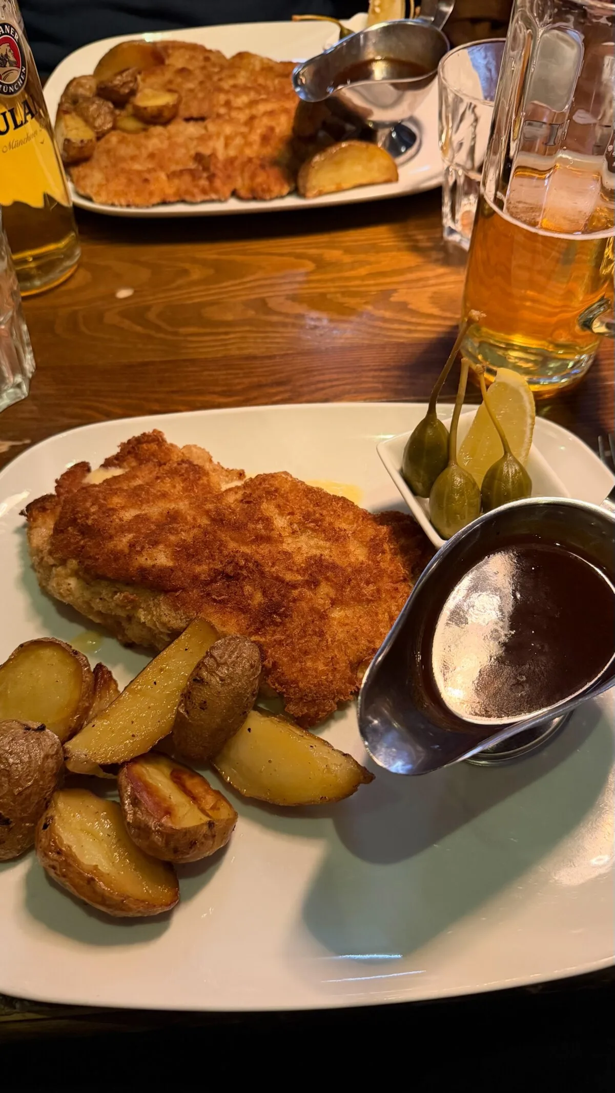 A huge breaded schnitzel with roast potatoes and sauce on a restaurant table in Stockholm