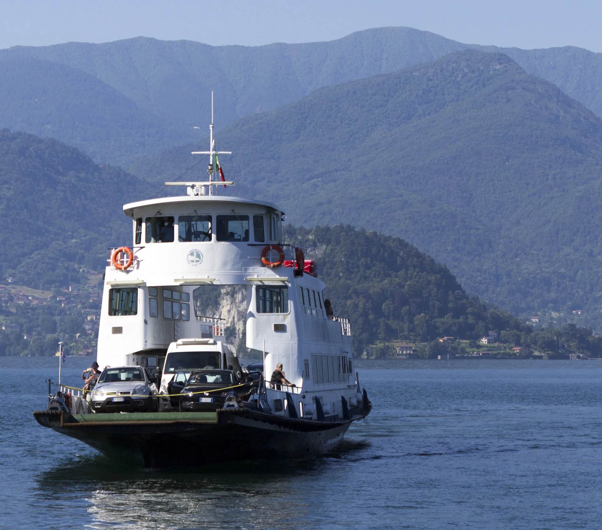 Ferry atracado en el muelle de Varenna en la orilla este del Lago Como con casas pastel detrás