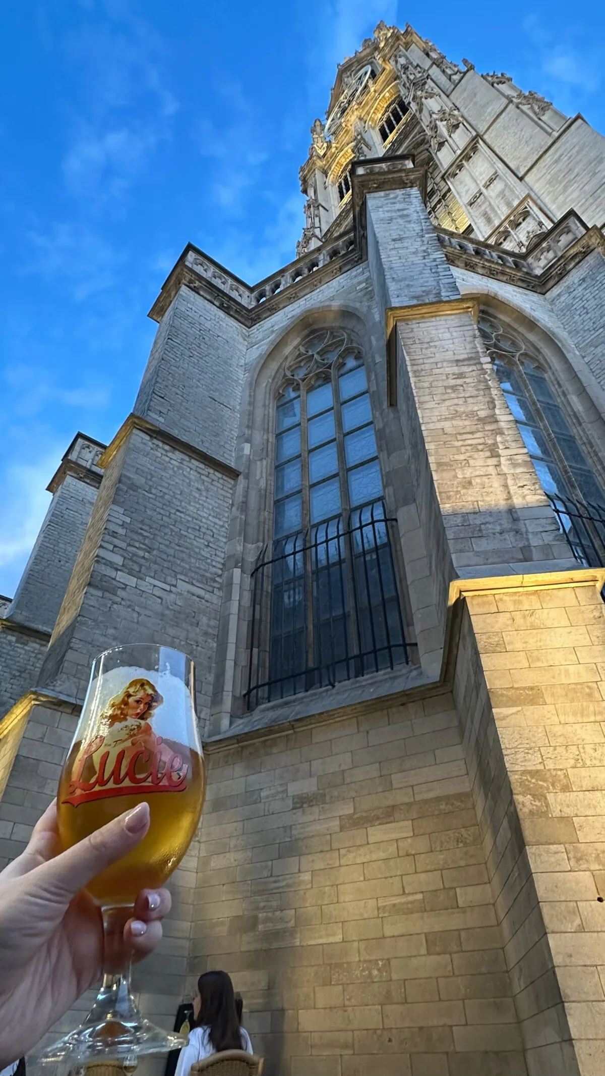 A glass of Belgian beer raised in front of the Cathedral of Our Lady in Antwerp