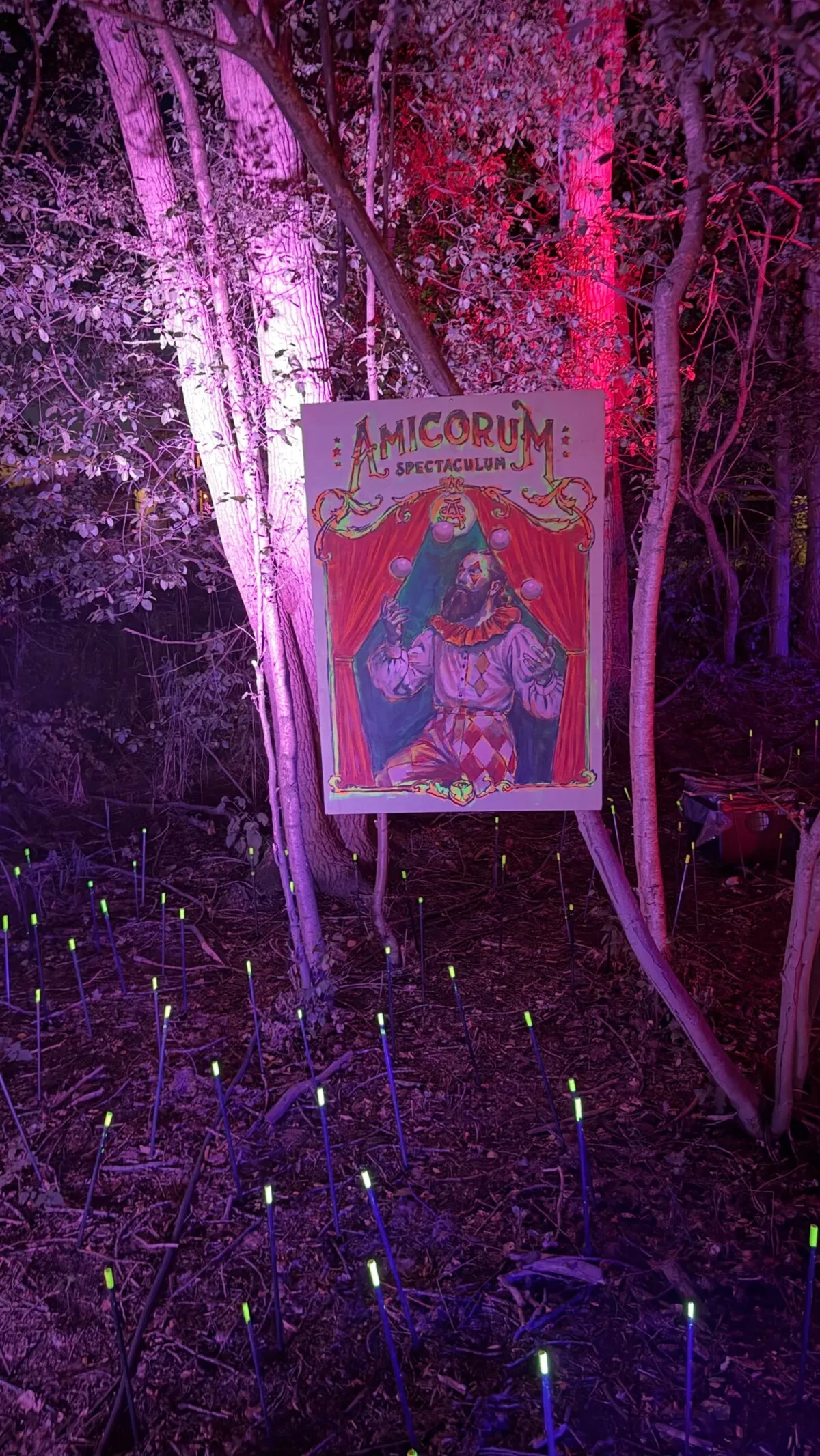 A glowing Tomorrowland sign lit in purple and pink among the trees of DreamVille at night